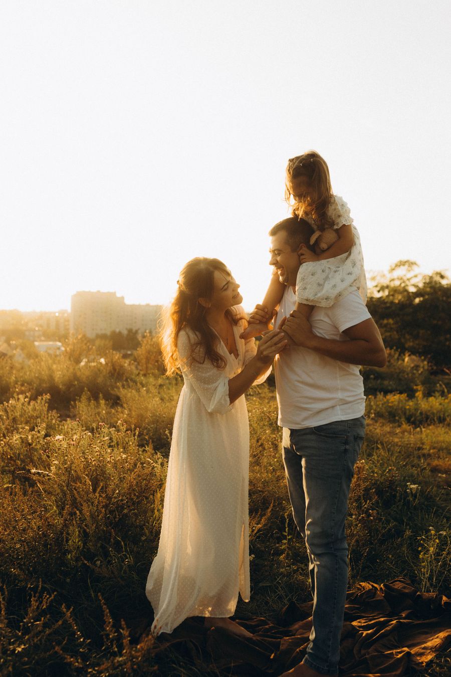 Two adults and a small child on their shoulders, standing in long grass in low golden sunlight.